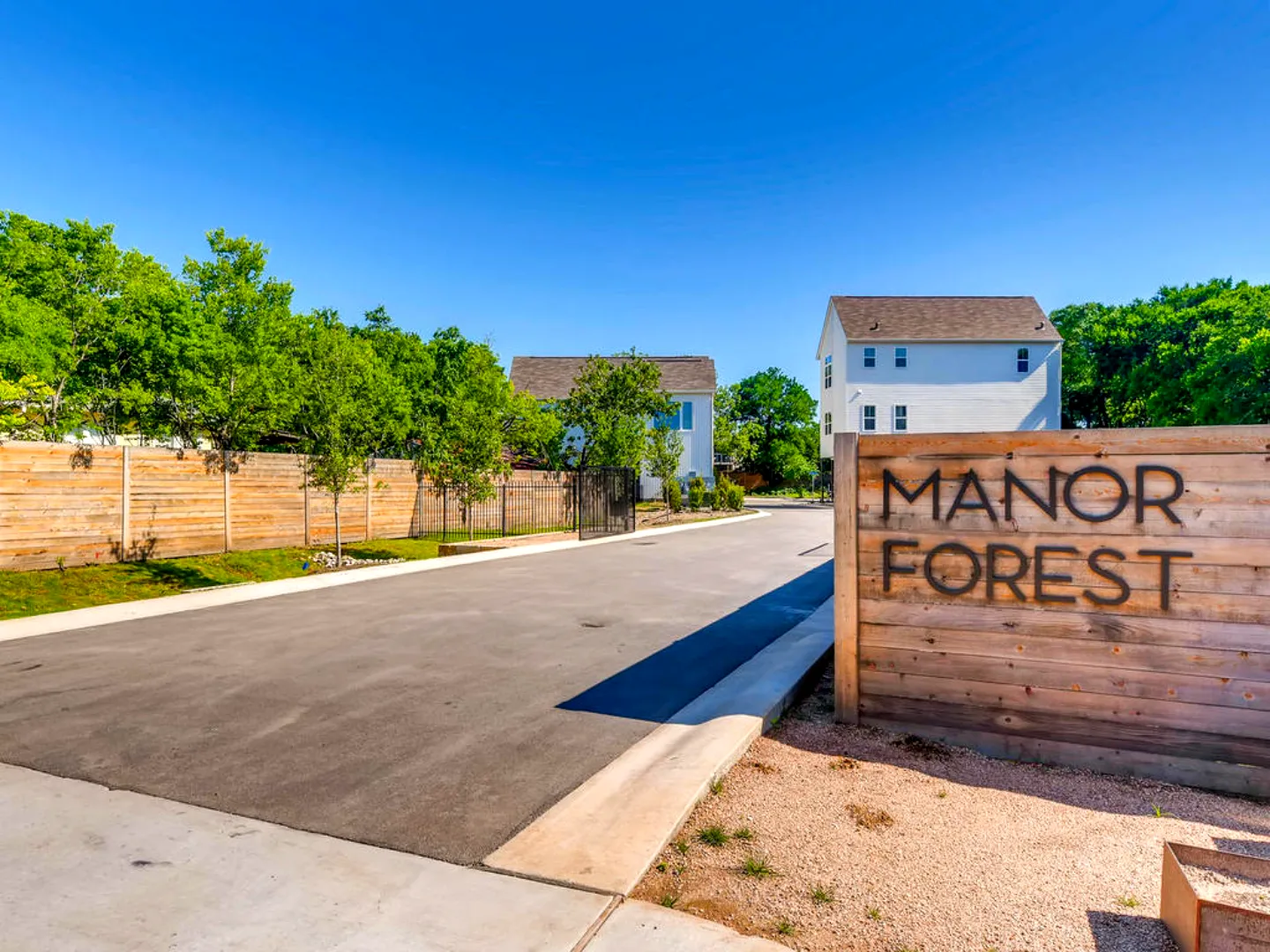 manor-forest-new-manor-web Entrance to the completed Manor Forest residential development in Austin, Texas, with the horizontal cedar monument sign, new private street, concrete curb and sidewalk, and two-story homes beyond on a site engineered by Mahoney Engineering.